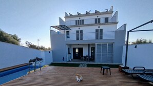 A modern two-story house with a wooden deck, a swimming pool, and a patio area with outdoor furniture. - DALT DES PADRÓ (Muro)