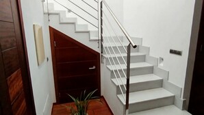 A staircase with a wooden door on the left and a potted plant at the bottom. - DALT DES PADRÓ (Muro)