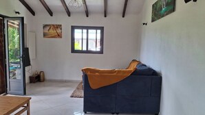 Una habitación con un sofá azul oscuro, una mesa de madera, una ventana con persianas y un cuadro en la pared.