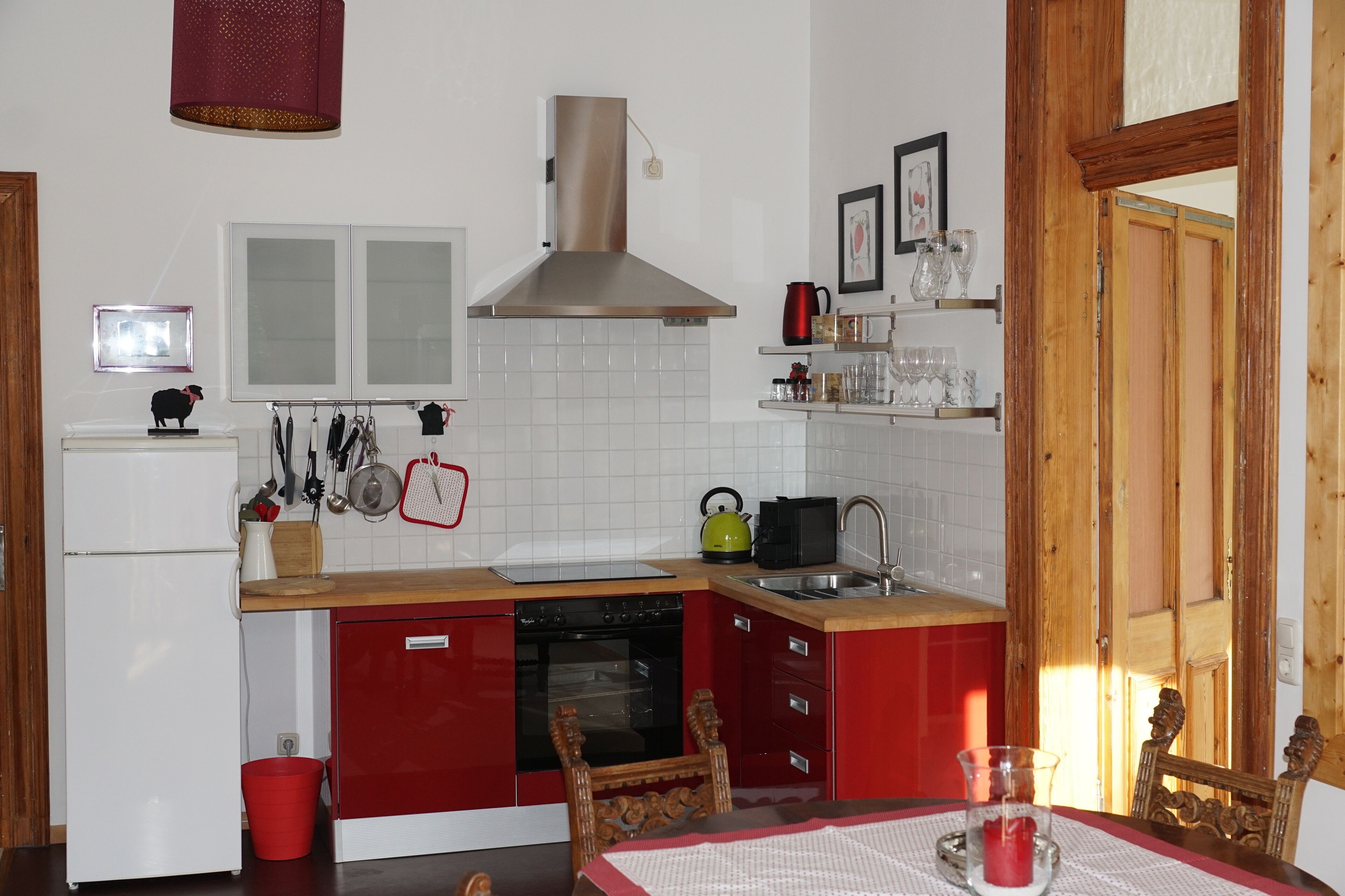 A compact kitchen with a red and white color scheme, featuring a stove, sink, and a red refrigerator.