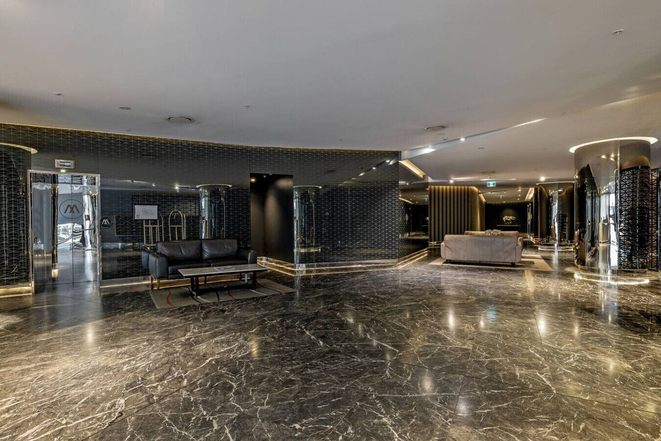 A modern lobby with a marble floor, a reception desk, seating area, and a large glass door.