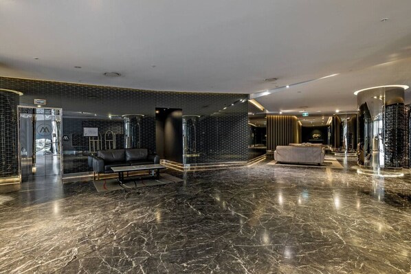 Un hall d’entrée moderne avec un sol en marbre, un comptoir d’accueil, un espace salon et une grande porte en verre.