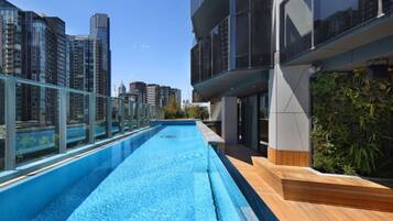A rooftop pool with a glass barrier, surrounded by high-rise buildings and a wooden deck.