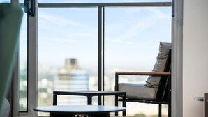 Habitación con vistas a un paisaje urbano a través de amplios ventanales, una silla y una pequeña mesa.