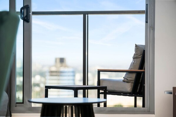 Ein Zimmer mit Blick auf eine Stadtlandschaft durch große Fenster, ein Sessel und ein kleiner Tisch.