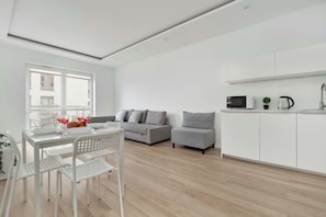 Um apartamento moderno com área de jantar, dois sofás cinzas, cozinha com armários brancos e uma janela grande.
