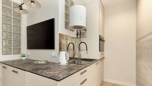 Een moderne keuken met een donker aanrecht, witte kasten, een grote flatscreen-tv en een inbouw afzuigkap.