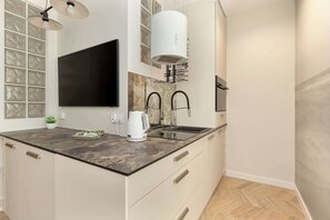 Una cocina moderna con encimera oscura, armarios blancos, un televisor de pantalla plana grande y una campana extractora integrada.