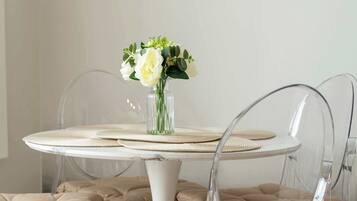 A round dining table with a clear glass vase containing flowers, clear chairs with cushioned seats, and woven placemats.