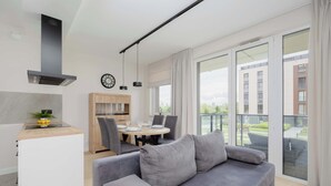 Un espace de vie moderne avec un canapé gris, une table à manger en bois et un coin cuisine doté d’une cuisinière intégrée.