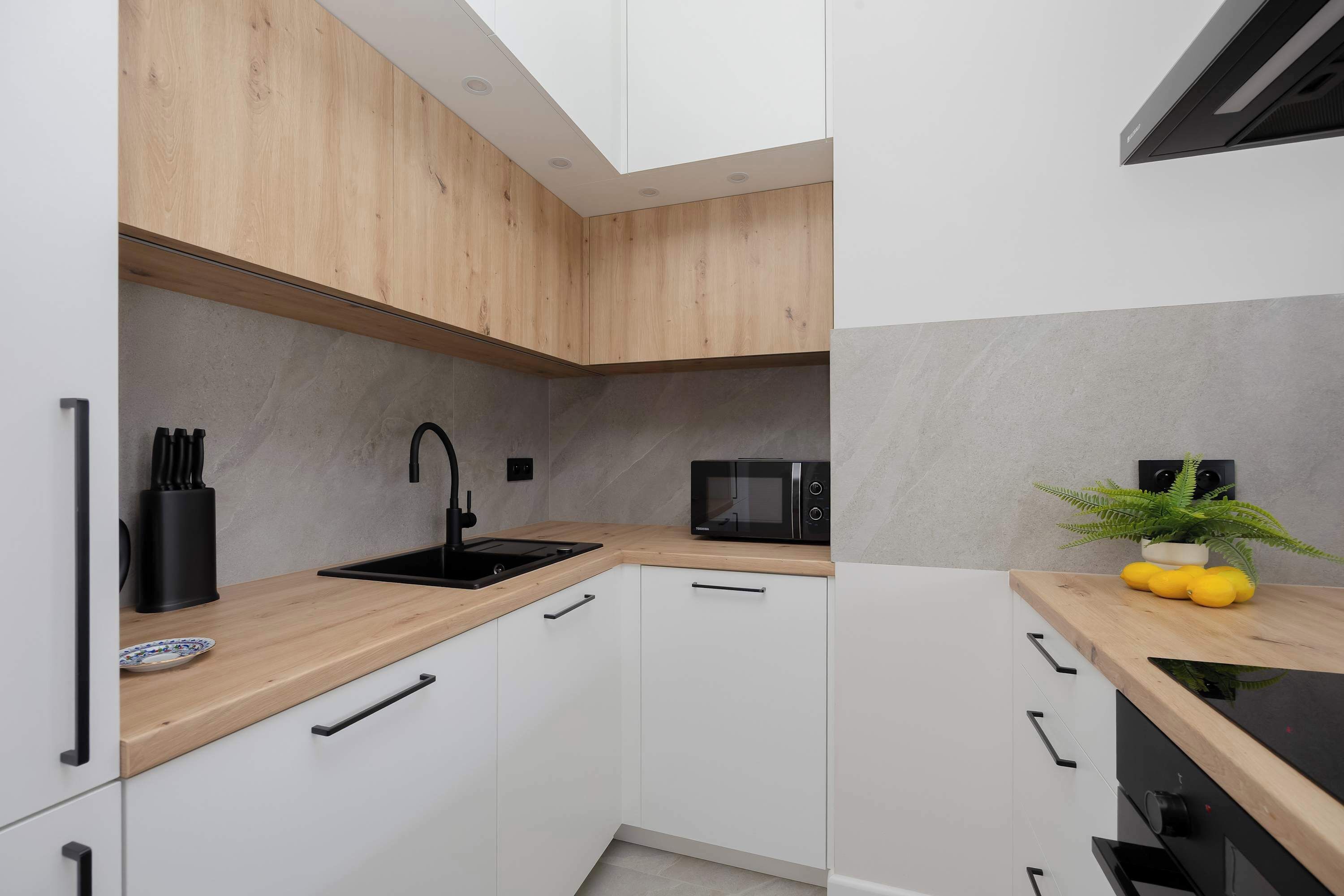 Eine moderne Küche mit weißen Schränken, einer Holzarbeitsplatte, einem schwarzen Spülbecken, einer Mikrowelle und einem Blumentopf.