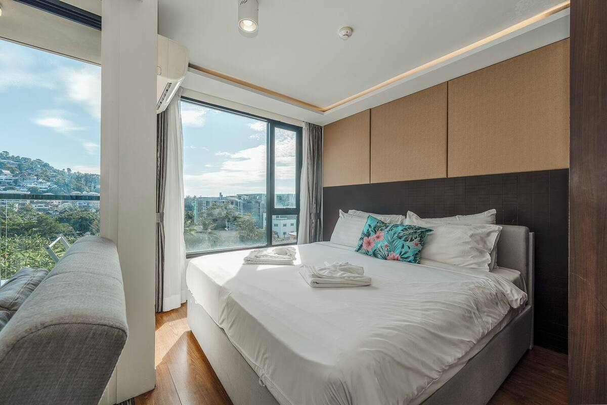A modern bedroom with a large bed, a view of the city, and a balcony.