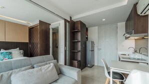 A modern living room with a grey sofa, a dining table with chairs, a kitchen area with a refrigerator, and a built-in wardrobe. - TheAristoLuxury Beach Resort Phuket C153 (Choeng Thale)