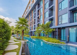 A modern hotel with a swimming pool, surrounded by greenery and a clear sky. - TheAristoLuxury Beach Resort Phuket C153 (Choeng Thale)