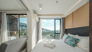 A hotel room with a large bed, a sofa, and a view of a cityscape through a large window. - TheAristoLuxury Beach Resort Phuket C153 (Choeng Thale)