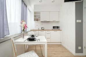 A modern kitchen with white cabinets, a microwave, and a dining area with a table and chairs. - Bright Studio in the Center of Wroclaw | Parking and Air Conditioning (Wrocław)