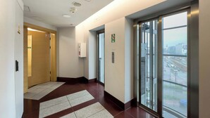 Un couloir avec une porte en bois, un ascenseur et une grande fenêtre donnant sur la ville.