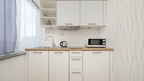 Une cuisine moderne avec des meubles blancs, un four à micro-ondes, une bouilloire et une fenêtre ornée de rideaux légers.