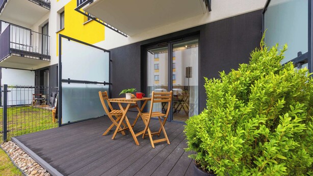 Un patio moderno al aire libre con una mesa y sillas de madera, una planta en maceta y un ventanal de vidrio que da a un espacio interior.