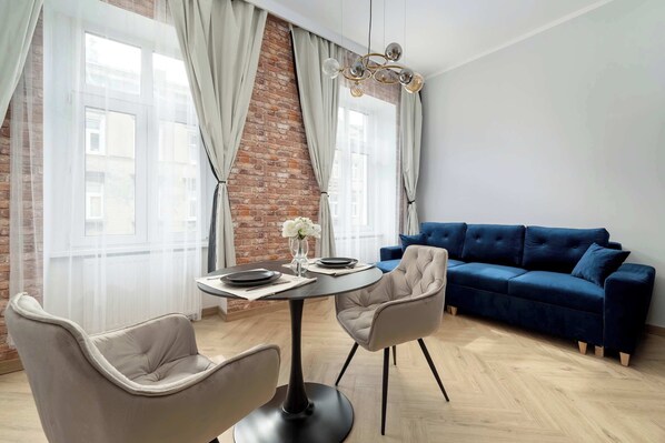 Una sala de estar moderna con una mesa de comedor redonda, dos sillas, un sofá azul y una pared de ladrillo.