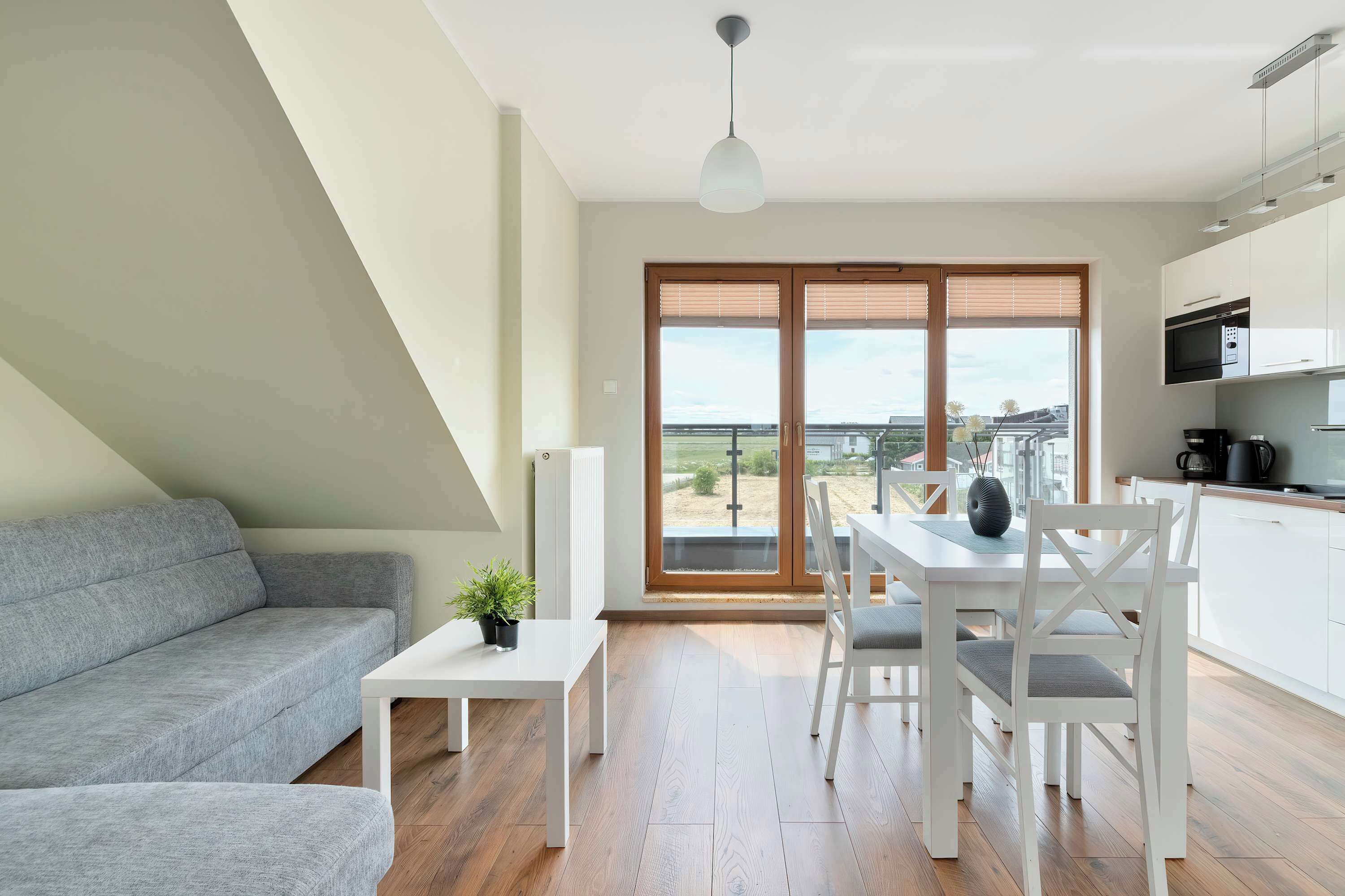 The living area with a bright kitchenette and dining space is filled with natural light streaming through large windows.