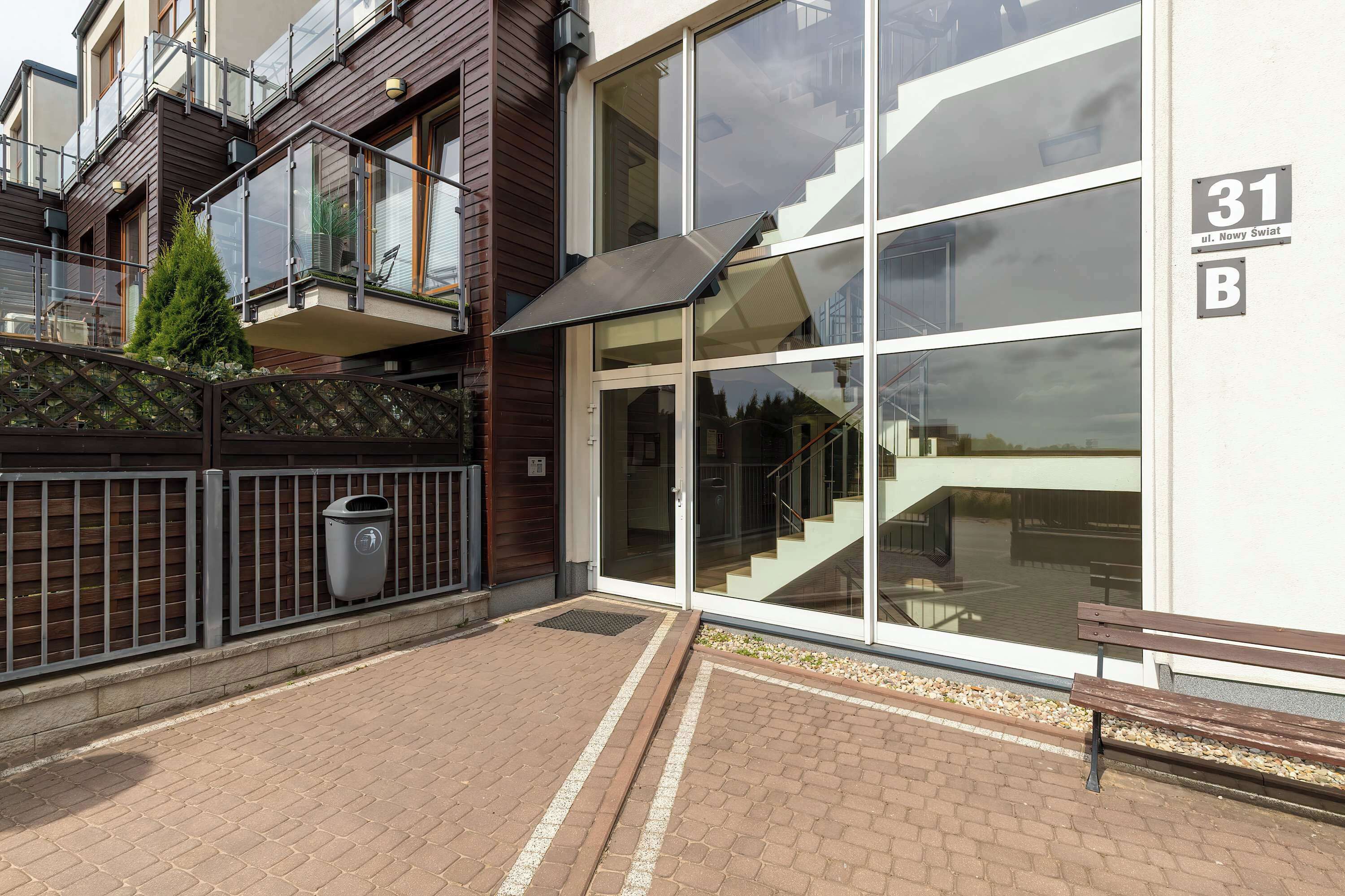 A modern building with large windows, a visible staircase, and a bench outside.