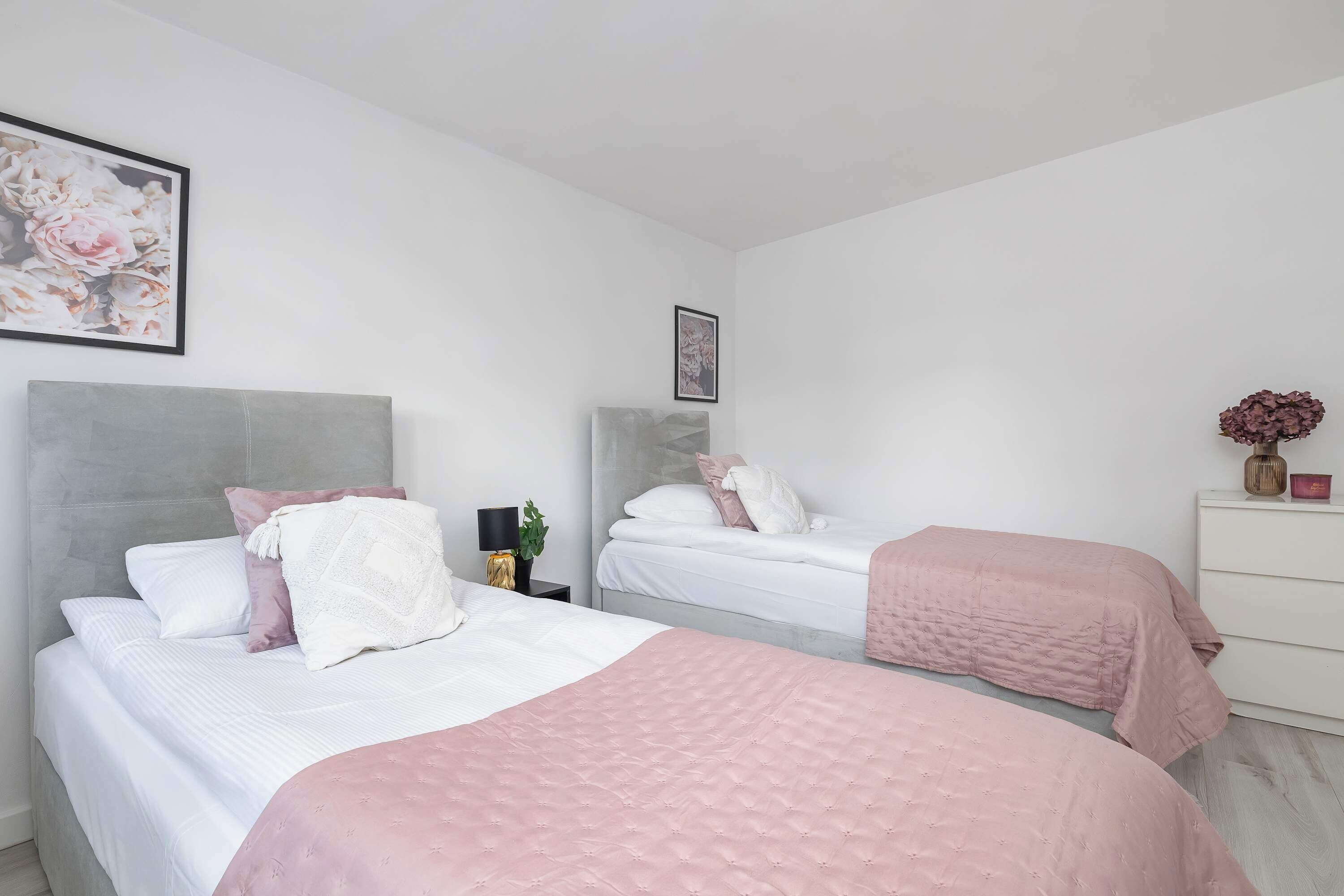 A bedroom with two beds, each with a headboard, a bedside table with a lamp, and a framed picture on the wall.