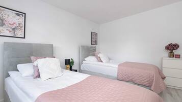 A bedroom with two beds, each with a headboard, a bedside table with a lamp, and a framed picture on the wall.
