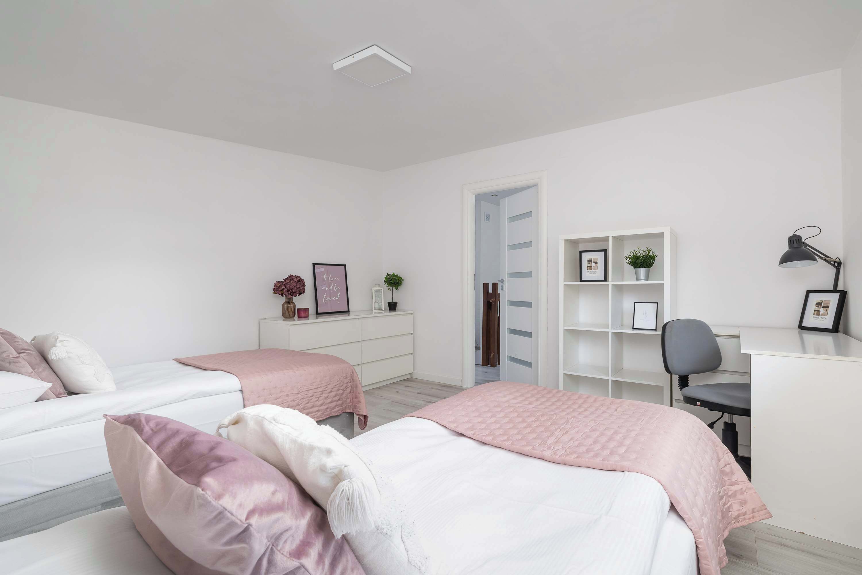 A modern bedroom with two beds, a desk, and a chair.