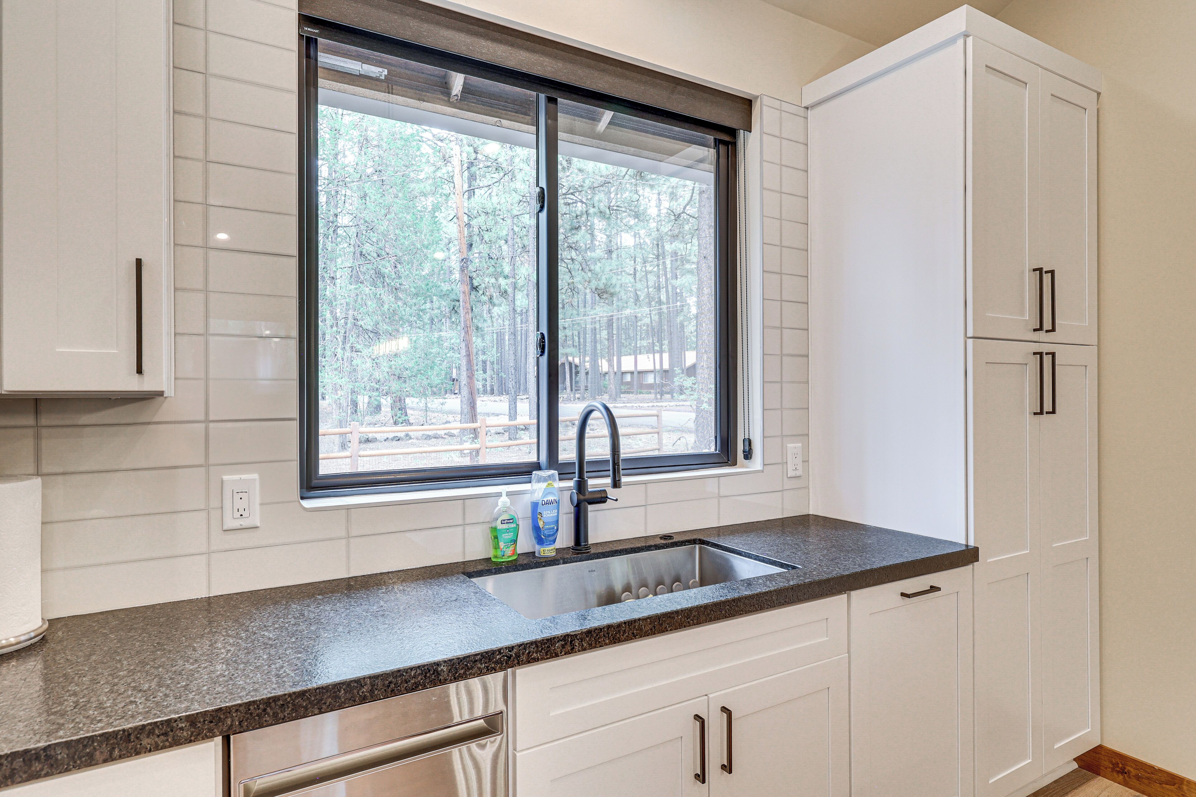 A kitchen with white cabinets, a granite countertop, a window with a view of trees, and a sink with a faucet.
