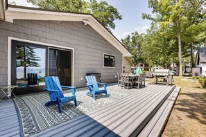 A deck with blue Adirondack chairs, a barbecue grill, and a dining table with chairs.