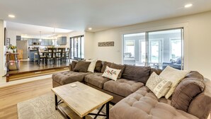 A modern living room with a sectional sofa, a wooden coffee table, and a dining area in the background. - Swim, Fish & Boat: House on Stunning Higgins Lake! (Roscommon)