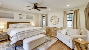 A bedroom with a bed, bedside tables, a ceiling fan, a sofa, a mirror, and a window with curtains. - Swim, Fish & Boat: House on Stunning Higgins Lake! (Roscommon)