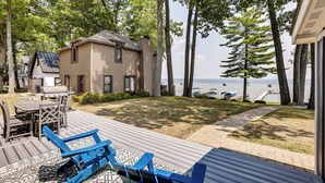 A house with a deck, outdoor furniture, and a view of the water. - Swim, Fish & Boat: House on Stunning Higgins Lake! (Roscommon)