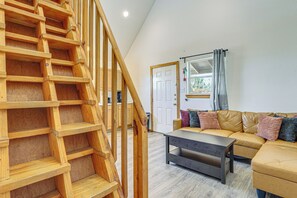 Een houten trap die leidt naar een slaapkamer op een entresol, met een bank en een bijzettafeltje in de woonruimte.