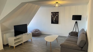 Un salon moderne avec un téléviseur à écran plat, un canapé gris, une table basse blanche et un fauteuil poire.