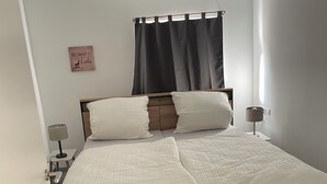 Une chambre à coucher avec un lit en bois, du linge de lit blanc, une lampe de chevet, une petite table et un élément de décoration murale.