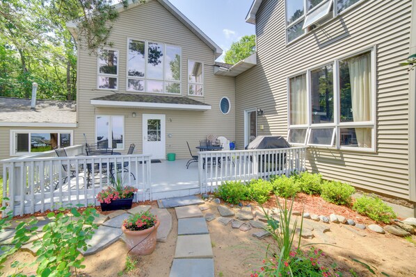 A two-story house with a covered patio, a white fence, and a garden with potted plants and stepping stones.