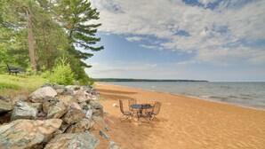 A beach with a table and chairs, a rocky area, and a bench. - Private Beach! Year-round Lake Superior Retreat (Big Bay)
