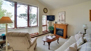 A living room with a fireplace, a sofa, a chair, a coffee table, and a television. - Private Beach! Year-round Lake Superior Retreat (Big Bay)