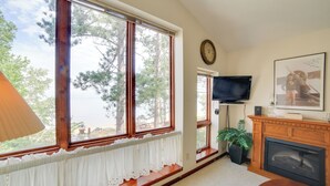 A living room with large windows, a fireplace, a television, and a framed picture on the wall. - Private Beach! Year-round Lake Superior Retreat (Big Bay)