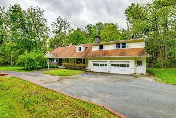 A two-story house with a garage, surrounded by lush greenery and trees. - Serene Home w/ On-site Brook in Callicoon Center (Roscoe)