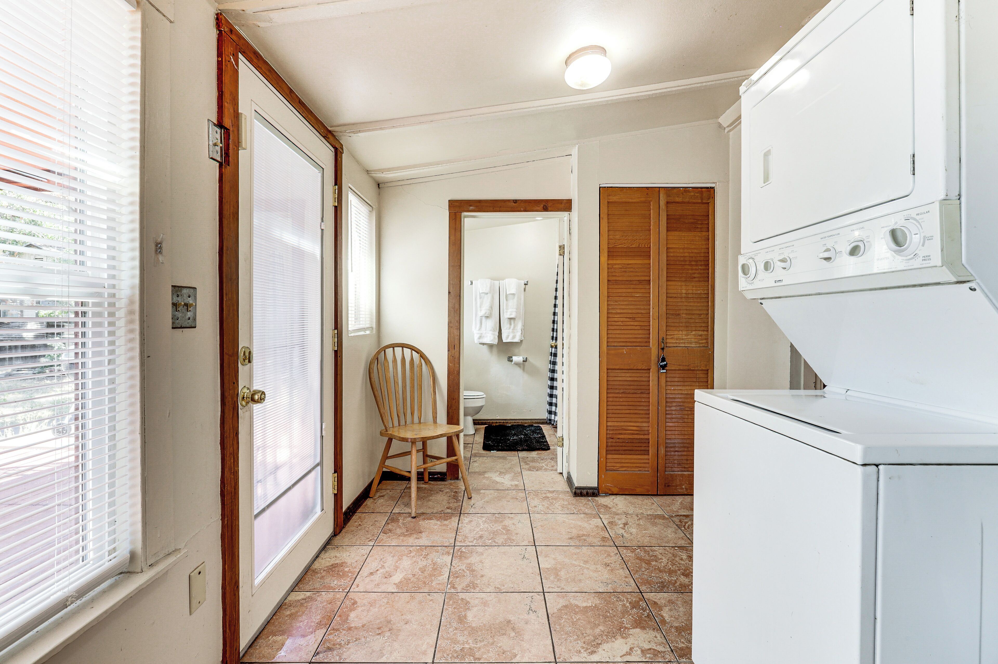 A laundry room with a washing machine, a chair, and a toilet.