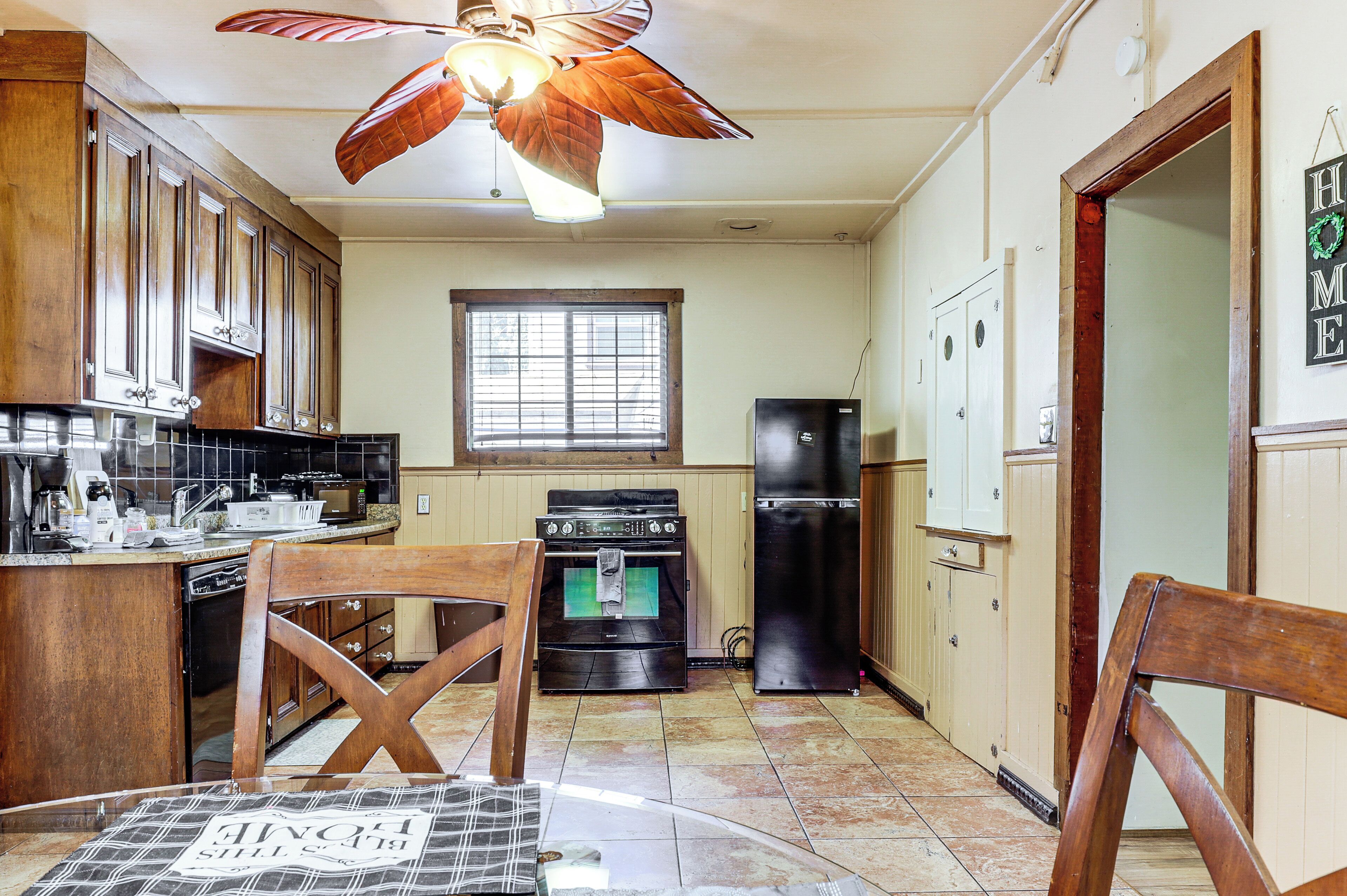 A kitchen with wooden cabinets, a black refrigerator, a stove, and a ceiling fan.