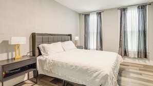 A neatly made bed with white linens, a bedside table with a lamp, and a window with curtains.