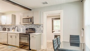 A modern kitchen with white cabinets, a microwave, a dishwasher, and a tiled backsplash.