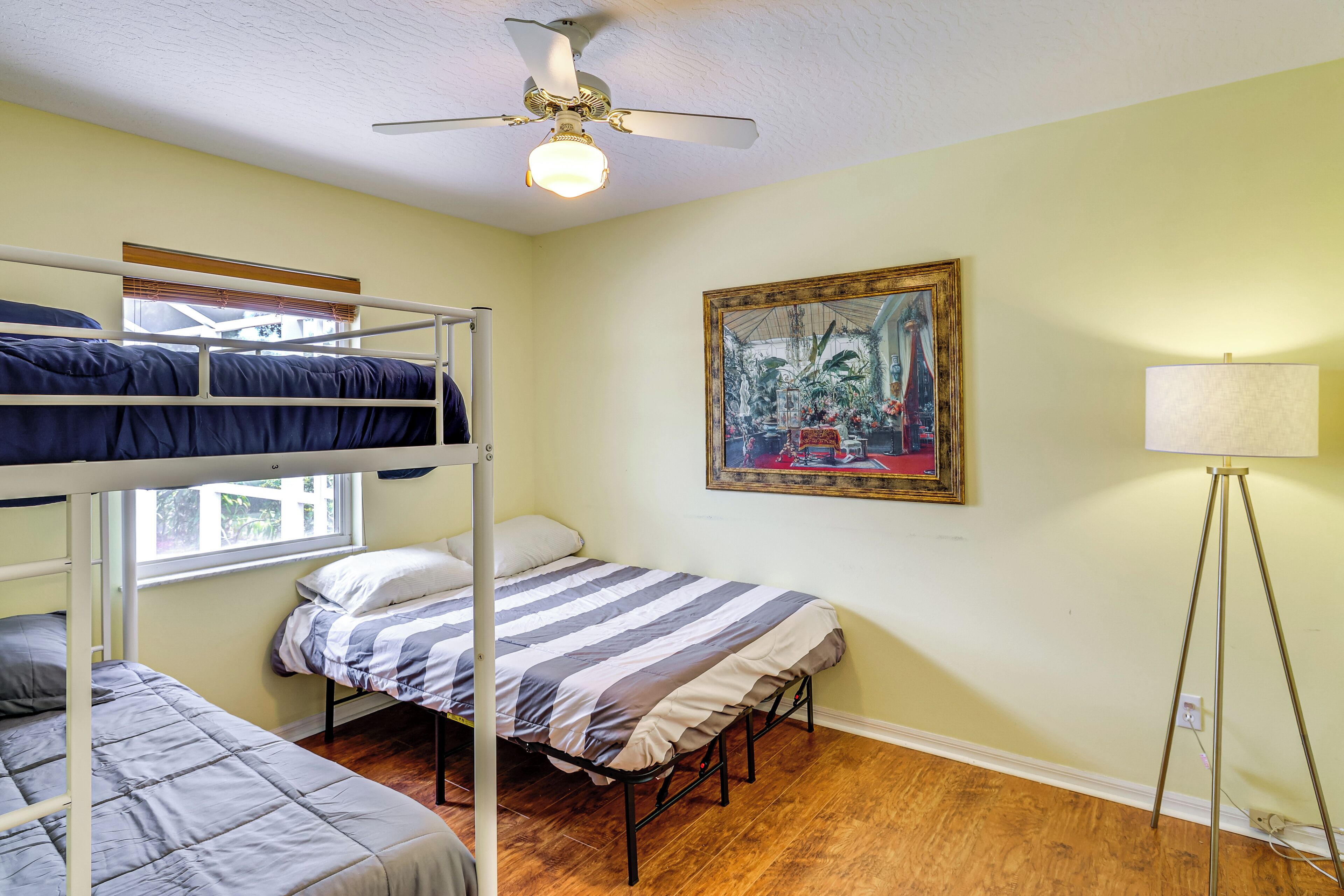 Ein Schlafsaalzimmer mit Etagenbetten, einem Deckenventilator, einem Bild an der Wand und einer Stehlampe.