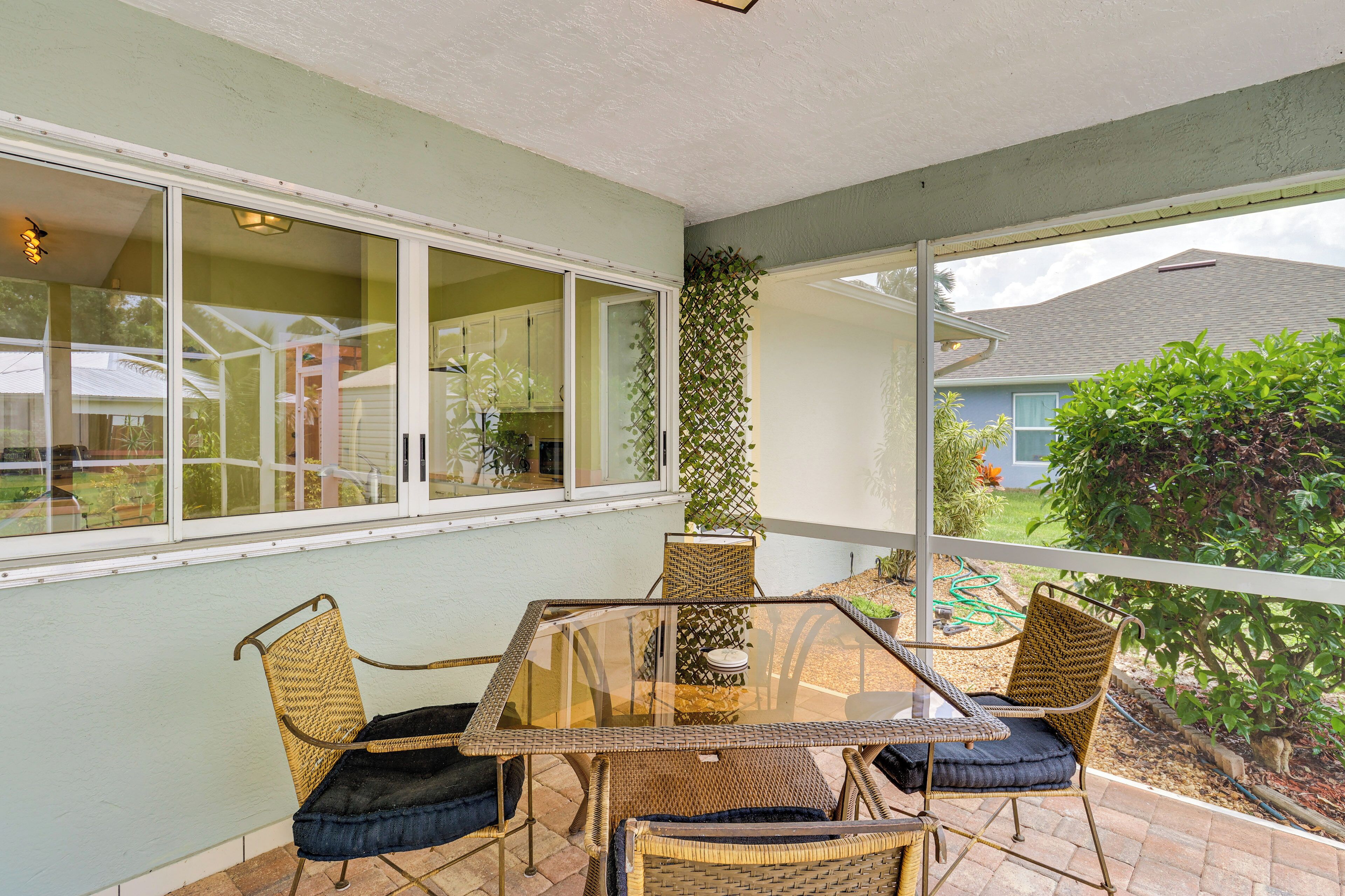 Une terrasse couverte avec une table en verre et des chaises en osier, donnant sur le jardin, et une porte-fenêtre coulissante qui mène à l’intérieur.