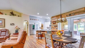 A spacious living room with a leather recliner, a dining area with wooden chairs and a table, and a kitchen with white cabinets and a refrigerator. - Welcoming Home w/ Yard on 20 Acres in High Springs (High Springs)