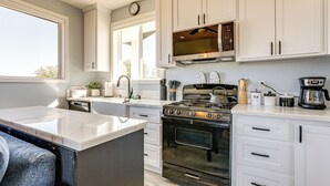 Une cuisine moderne avec des meubles blancs, une cuisinière, un four, un four à micro-ondes et une grande fenêtre.